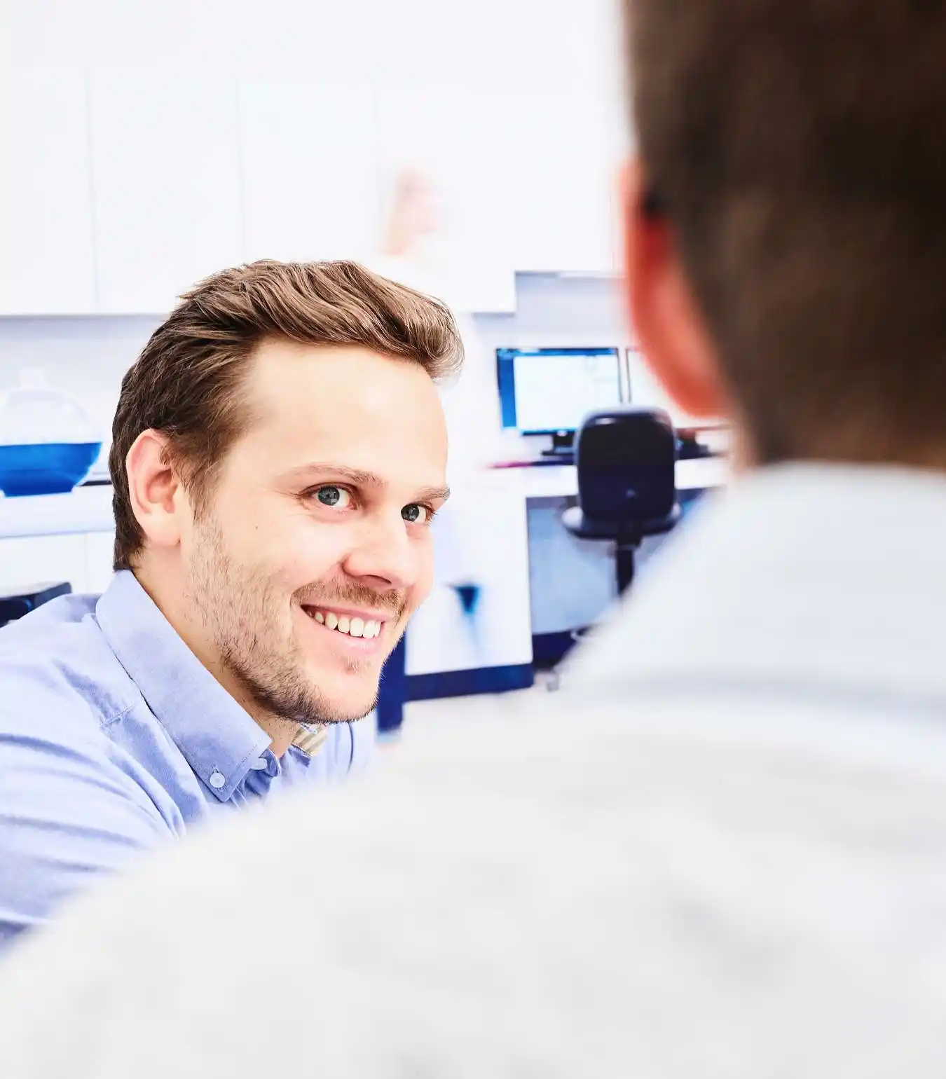 A photograph of a scientist smiling at another scientist in a lab