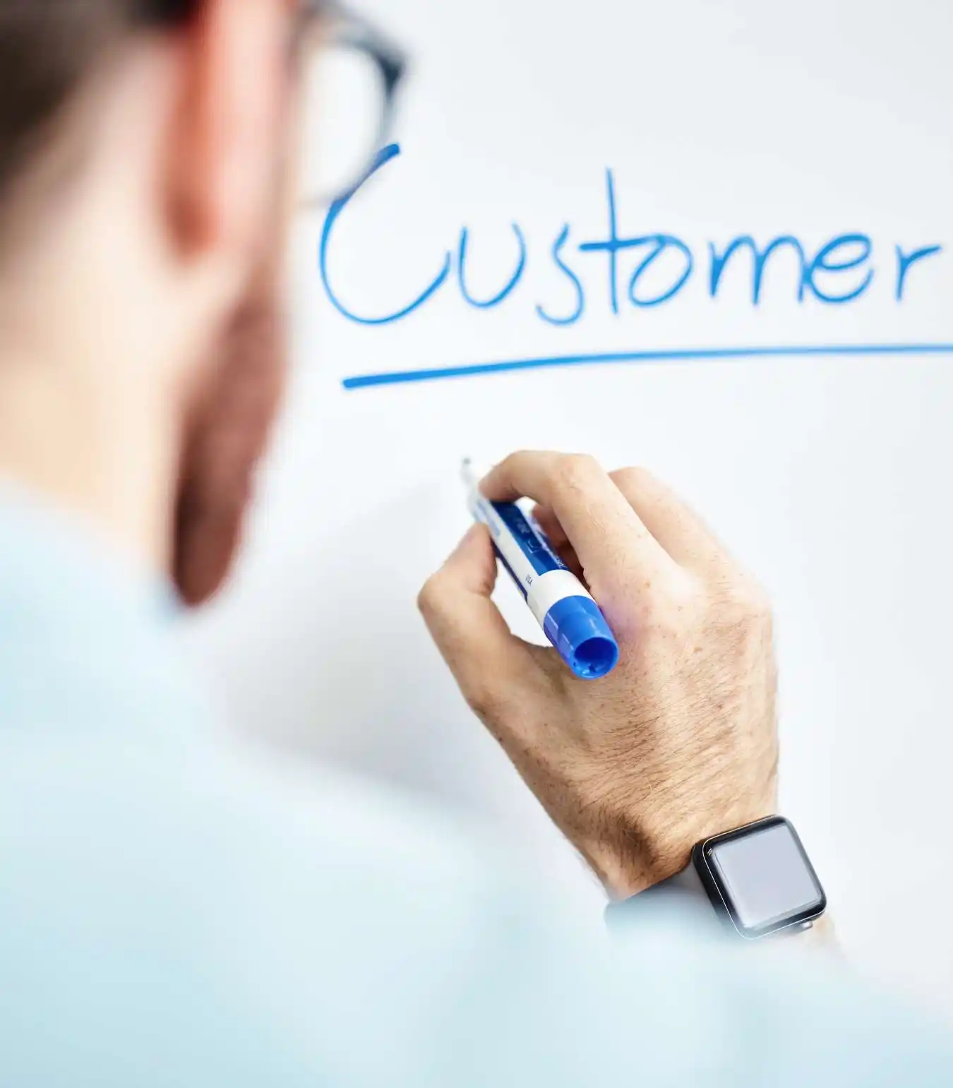 A photograph of someone writing "customer" on a whiteboard with a blue marker