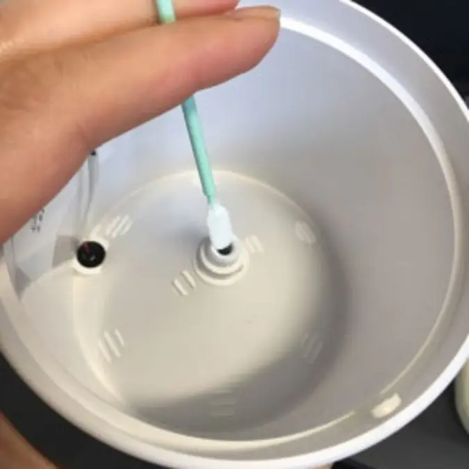 A photograph of someone using a cleaning swab to clean the bottom of the nozzle
