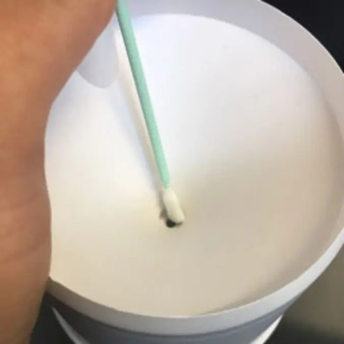 A photograph of someone using a cleaning swab to clean the top of the nozzle
