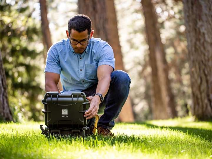 A photograph of a researcher in a forest setting up a SATURO infiltrometer