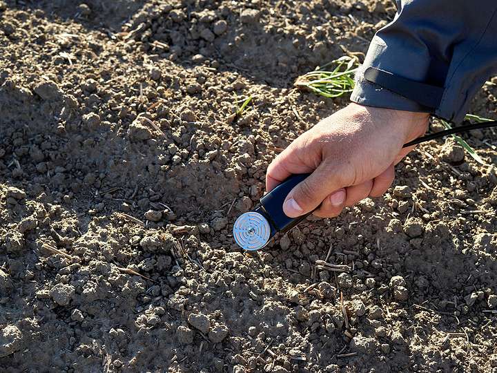A photograph of a research scientist holding a TEROS 21 sensor over rows of soil in a field