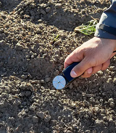 A photograph of a research scientist holding a TEROS 21 sensor over rows of soil in a field