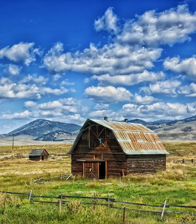 Image of an old barn and the field with a wooden fence with a blue sky dotted with clouds