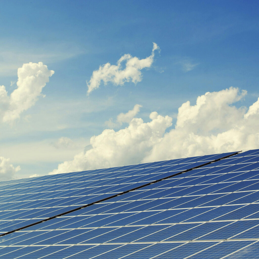 A photograph of a photovoltaic solar panel array with a bright blue sky wit wispy clouds